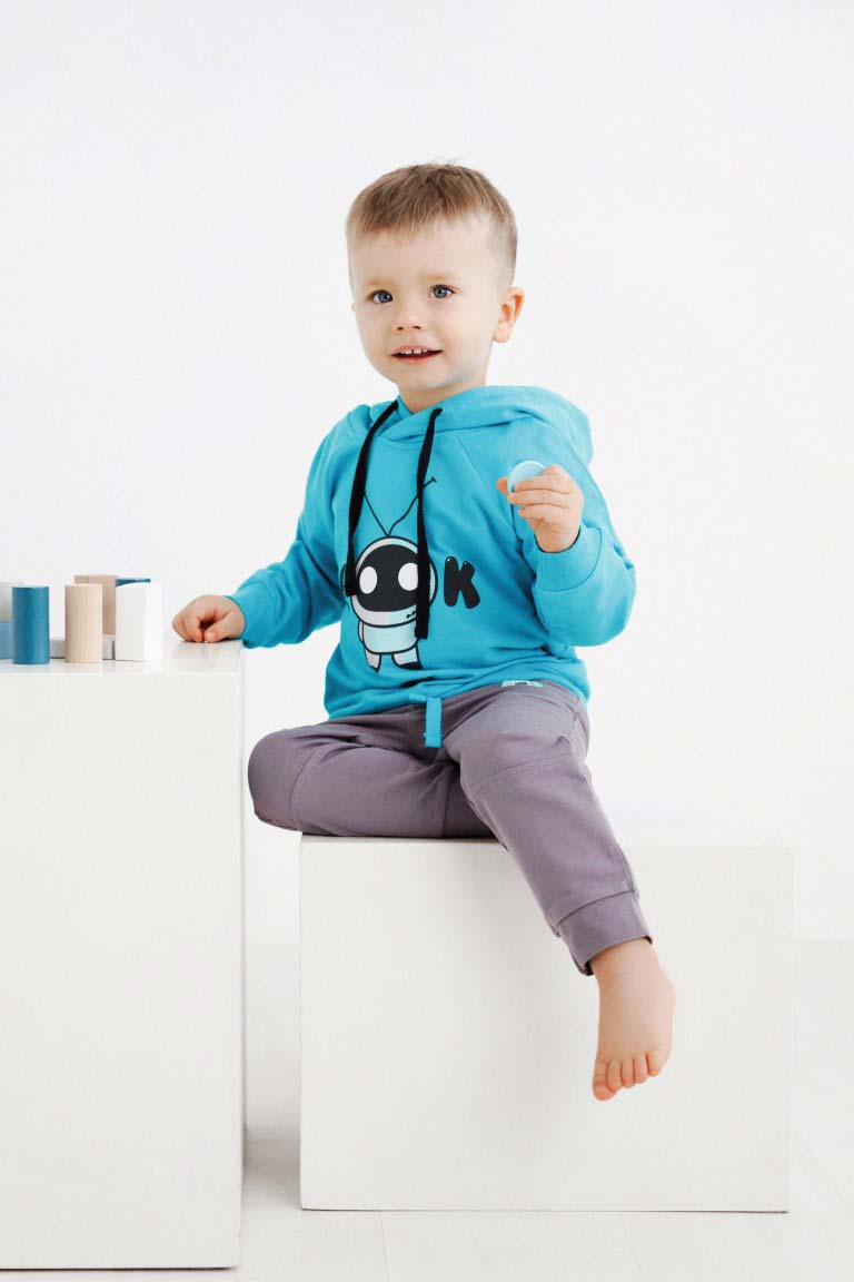 Cute boy wearing baby jumper Robot 232 and sitting on a white cube.