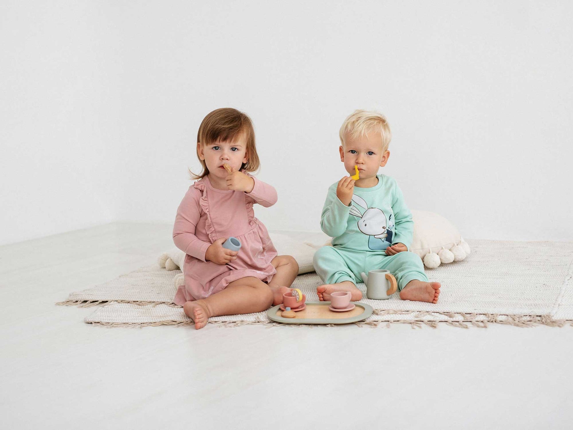 Two cute kids, a girl and a boy, the boy (riht) wears newborn pajamas Bear and Bunny 381, while the girl (left) wears a baby dress from our collection, baby dress Squirrel 360