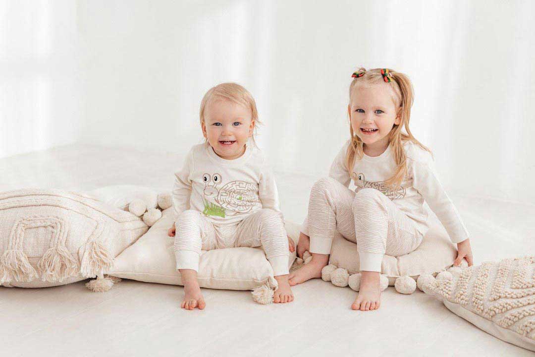 Two cute kids, a boy and a girl, sitting on cushins and wearing newborn pajamas Snails 300